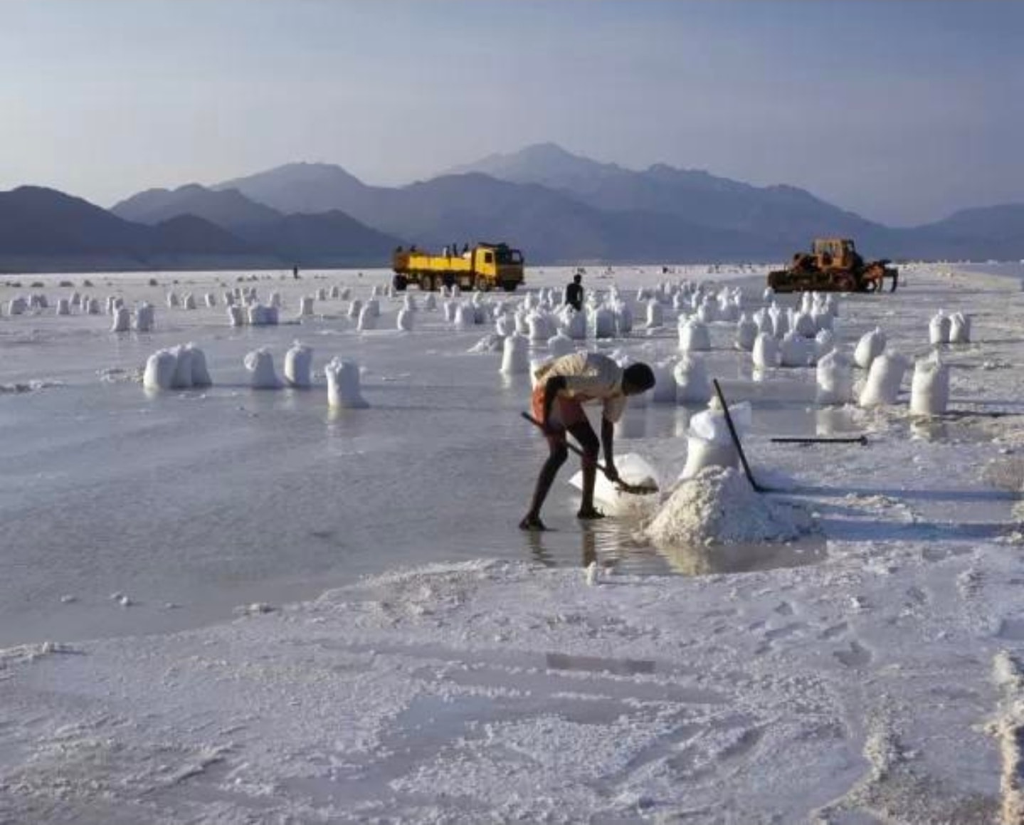 Wide view of the Lac Assal salt flat — white crystalline expanse with mountains and trucks